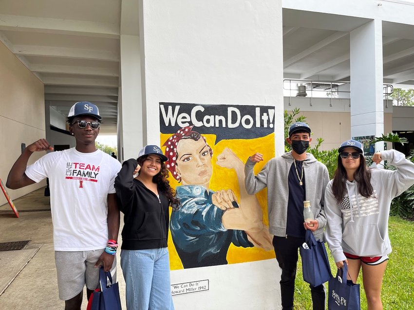 Ted B., Liliana S., Fabian E., and Jenesis S. Pose with a mural of Rosie the Riveter during their tour of Santa Fe College.